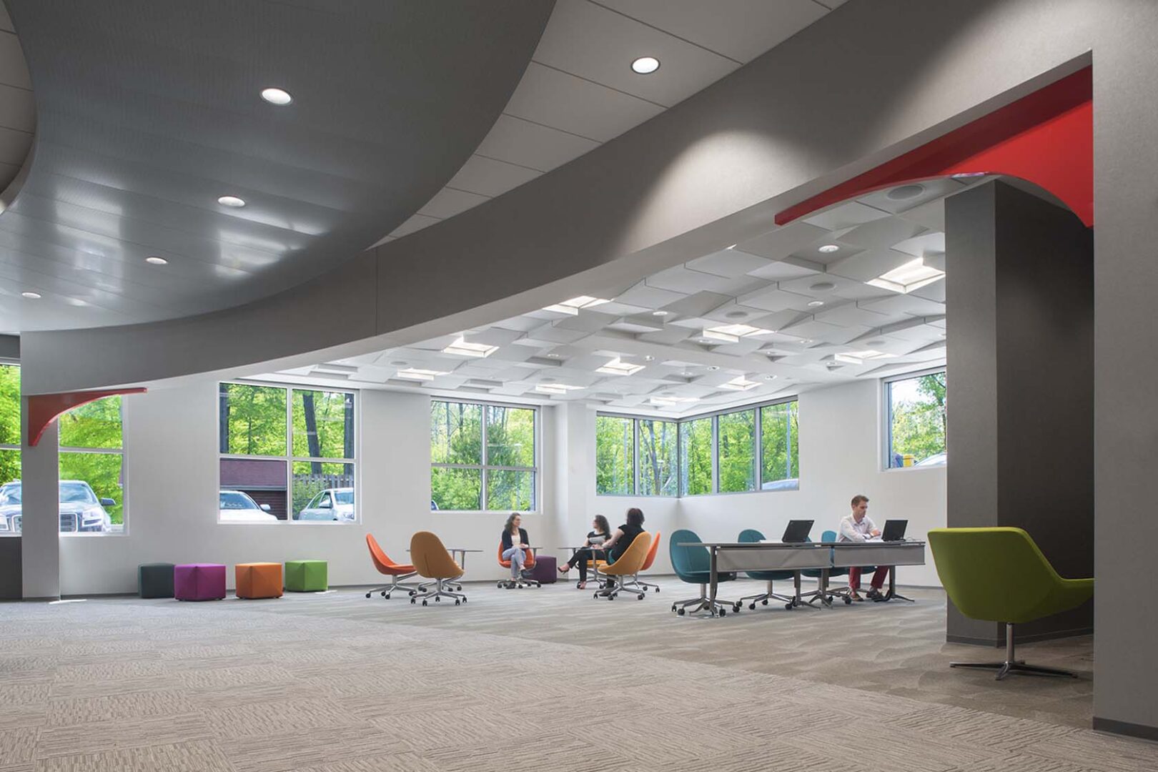 A group of people gathering in different clusters in mobile furniture in a room with windows